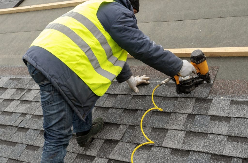 Workman using pneumatic nail gun install tile on roof of new house under construction