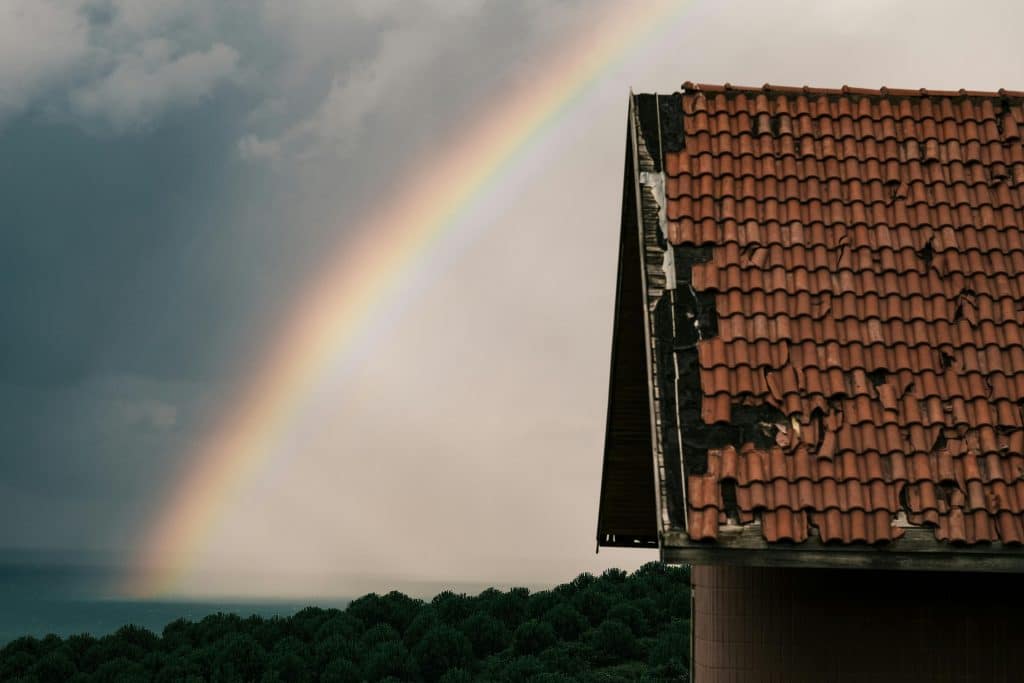 A damaged roof with a rainbow in the background